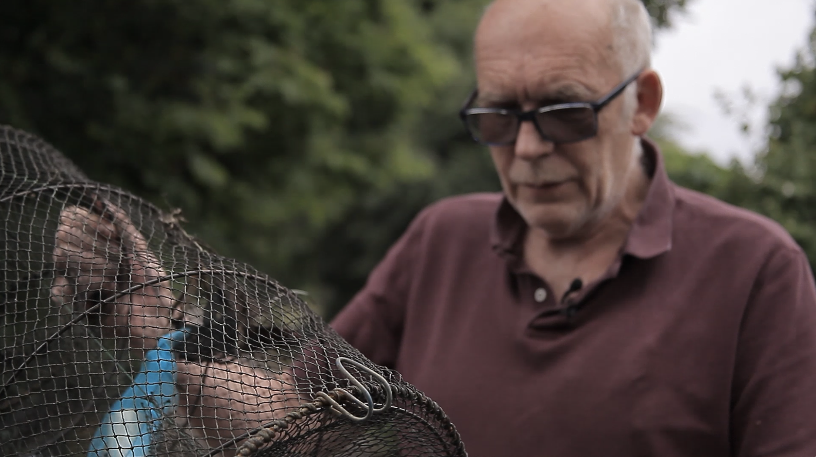 Bob Ring holds a crayfish trap, a black net stretched by a collapsible wire cylinder.