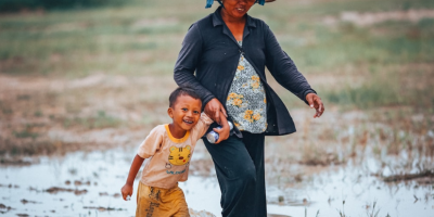 Image of a woman holding her son's hand while walking through a rice paddy. Photo by Mi Pham via Unsplash.