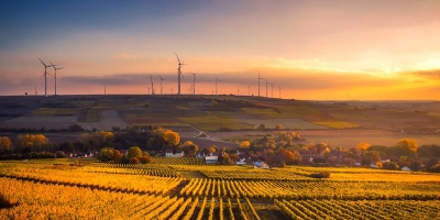 A farm at sunset with wind turbines in the background. Photo by Pixabay from Pexels