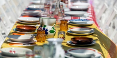 A long table full of colorful empty plates and cups on a colorful tablecloth flanked by white folding chairs. Photo by Mario Caruso via Unsplash.