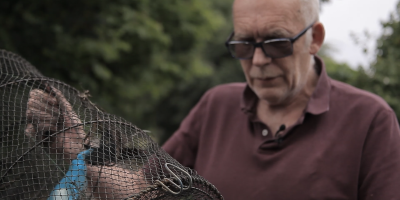 Bob Ring holds a crayfish trap, a black net stretched by a collapsible wire cylinder.