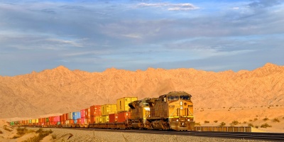A train carrying many shipping containers through a desert landscape. Photo by jdblack via Pixabay. 