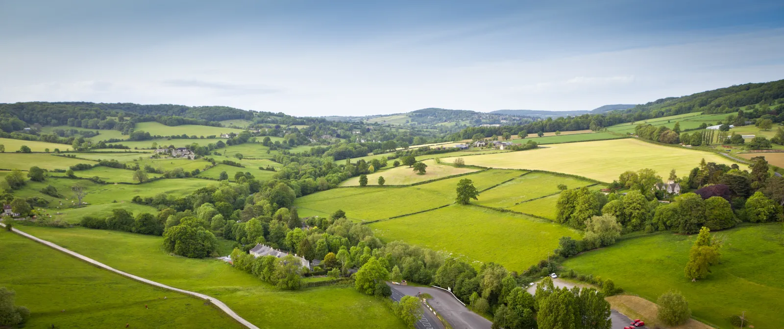 A green valley in the UK with green trees and agricultural lands with a road running through the middle.
