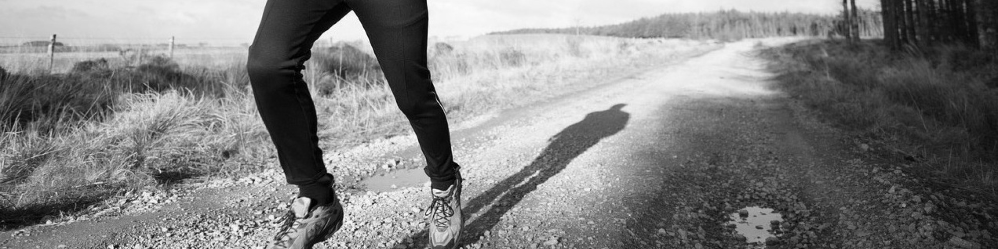 A photo in black and white of a man's shoes while running on a dirt road.