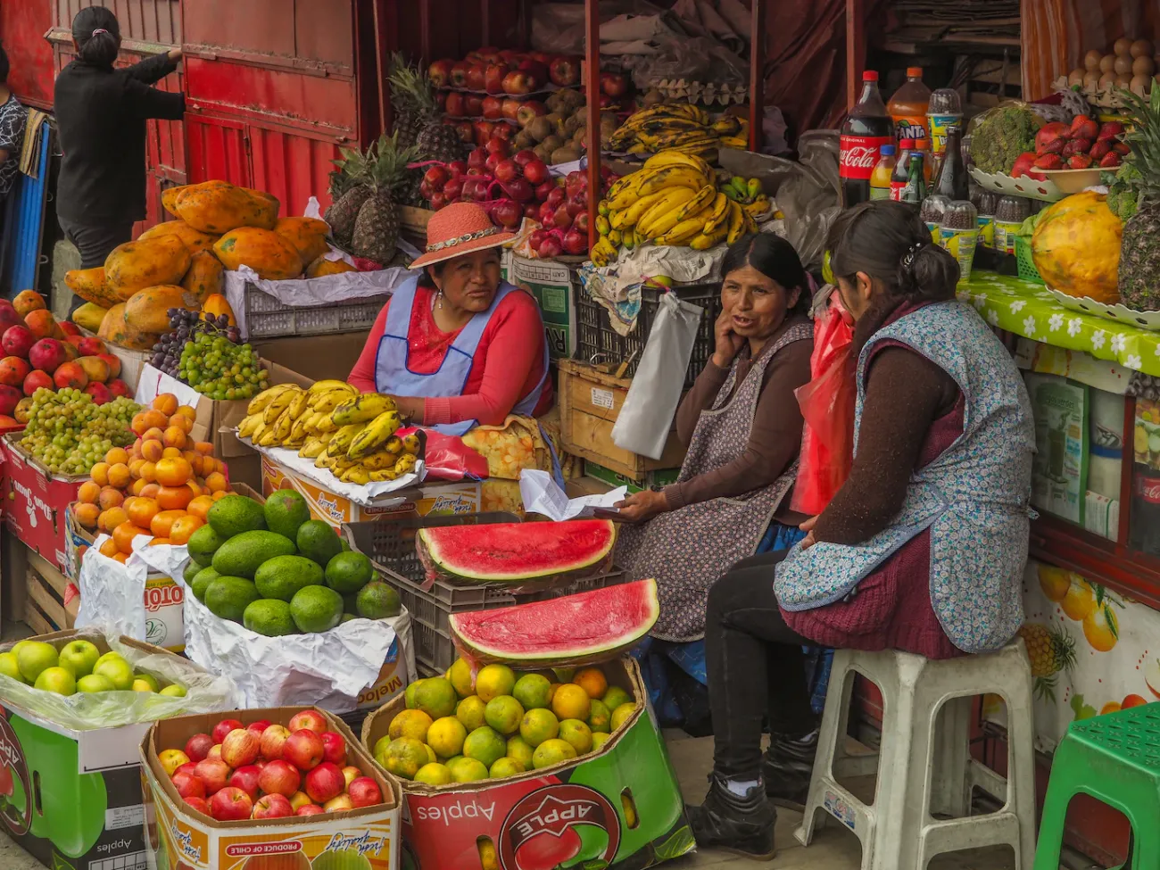 Three women sit at a market stall selling fruit in La Paz, Bolivia. Image credits: Lesly Derksen, Unsplash, Unsplash Licence.