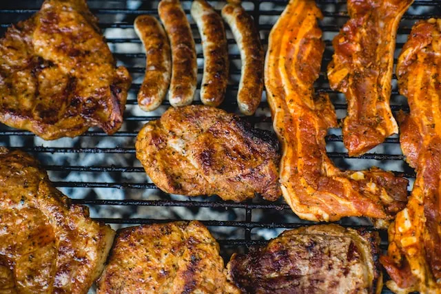 Chicken, bacon, and sausages cooked on a barbeque. Photo by Marcus Spiske via Unsplash.