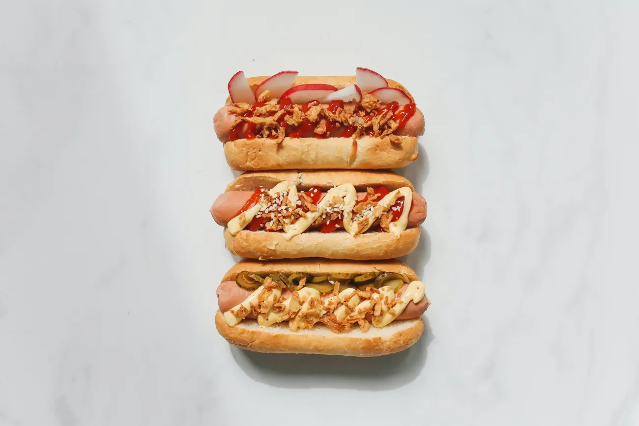 Image of three hot dogs with various toppings on white surface. Photo by Polina Tankilevitch via Pexels.