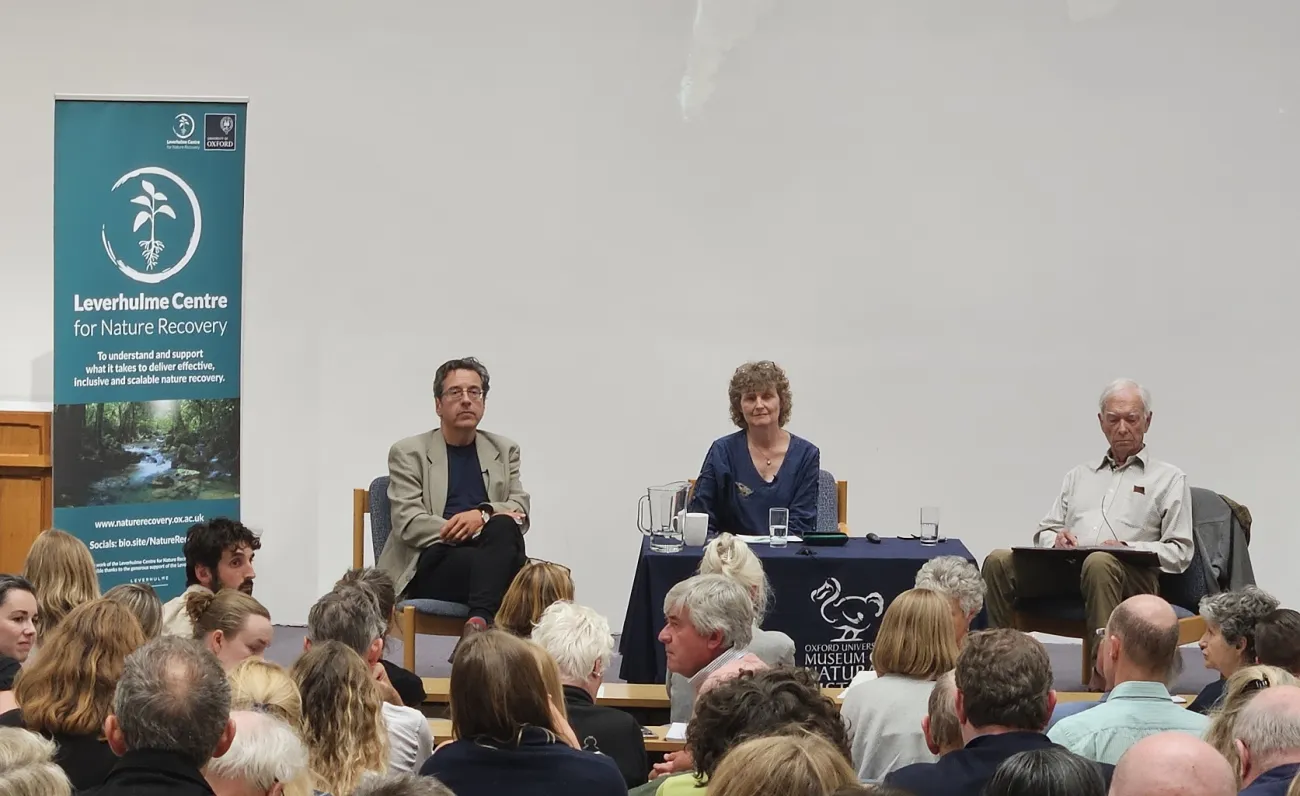 A banner for the Leverhulme Centre for Nature Recovery sits on the stage inhabited by George Monbiot, EJ. Milner-Gulland, and Allan Savory.
