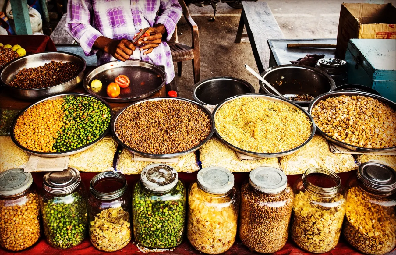 Clear glass jars and metal bowls full of colorful dried beans and peas sit on a table at a market in Bankok, Thailand. Photo by NEOSiAM 2021 via Pexels.