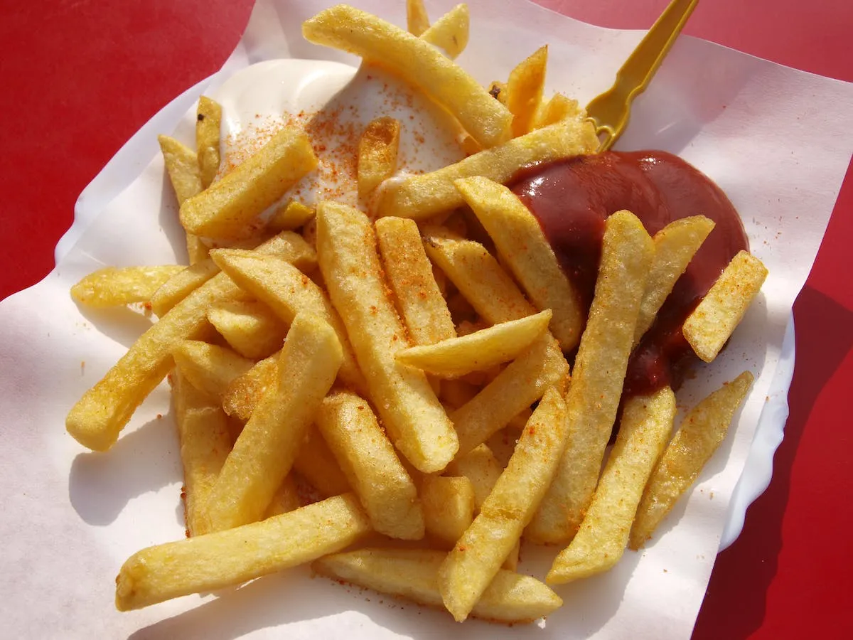 Photo of chips with ketchup and mayonnaise on white paper with red background. Photo by Marco Fischer via Pexels.