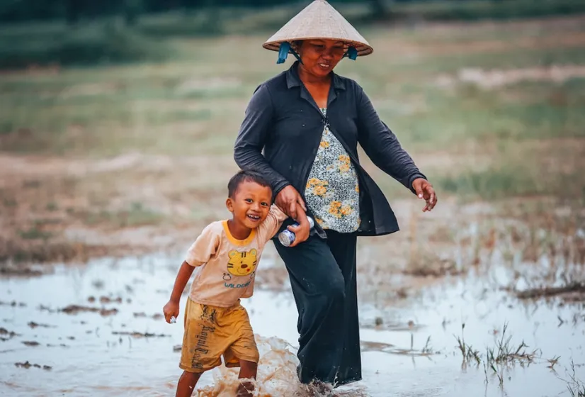 Image of a woman holding her son's hand while walking through a rice paddy. Photo by Mi Pham via Unsplash.
