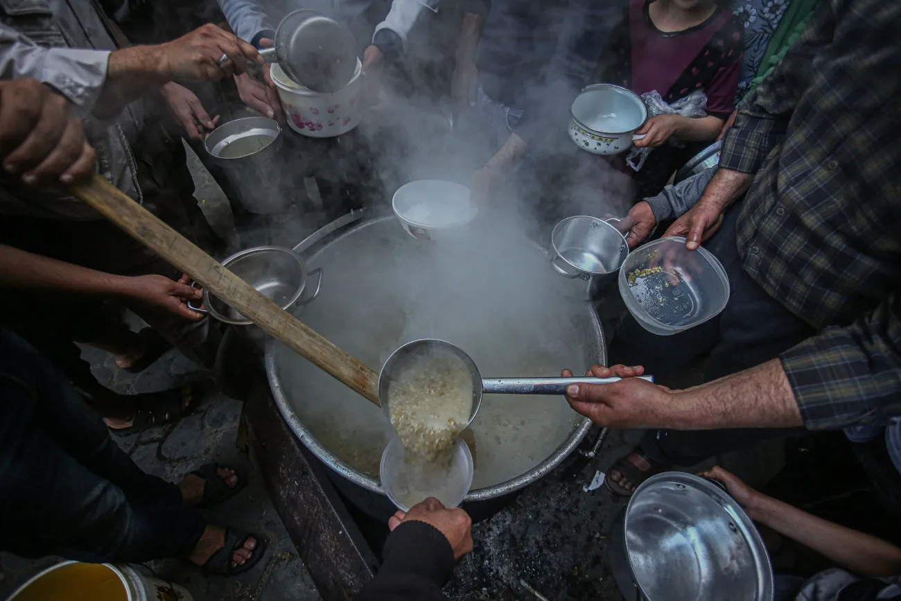 Photo of food being laddled from a large pot, surrounded by hands holding empty bowls in Gaza. Image by Yousef Masoud via Pixabay.