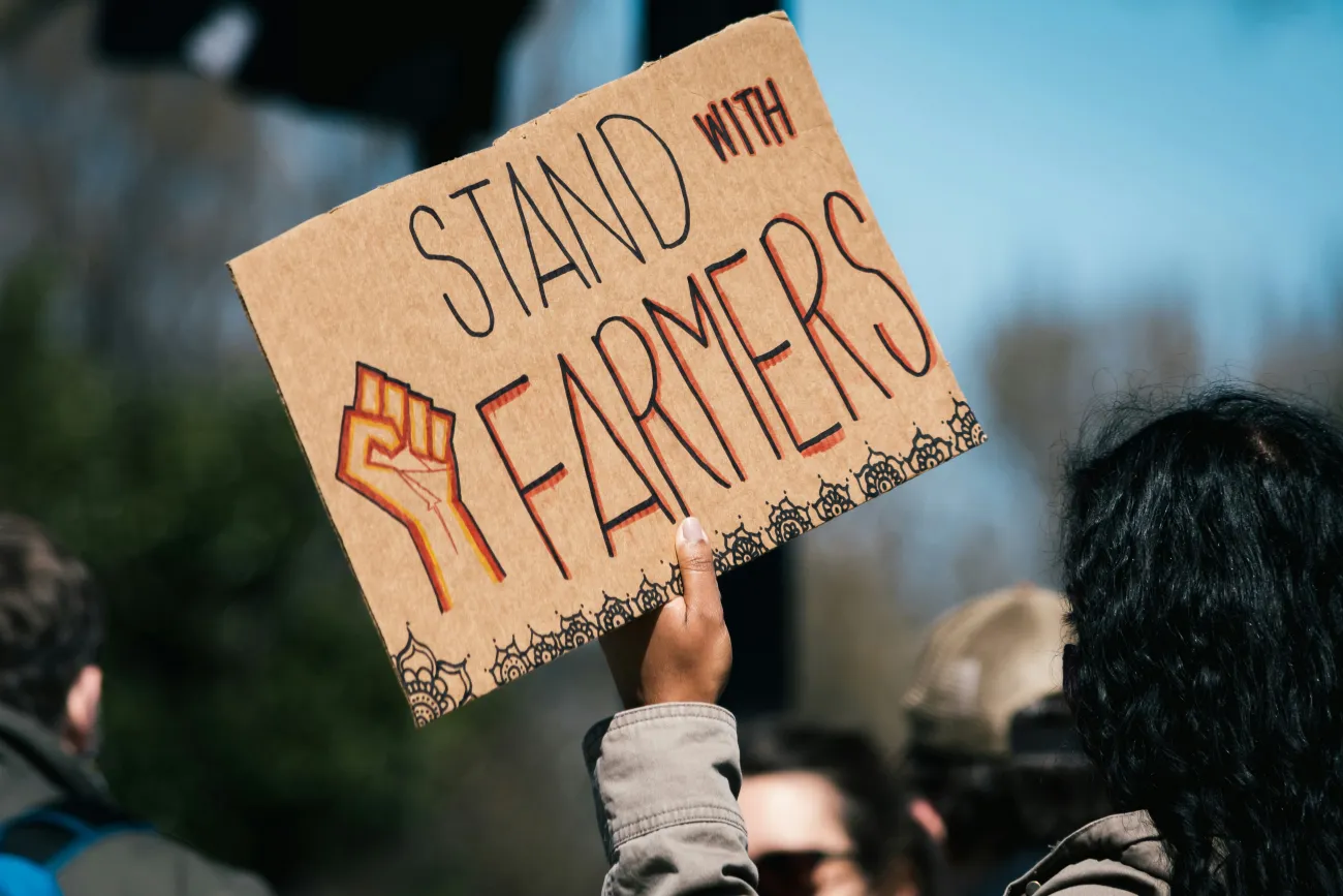 Photo of a protest sign which reads “Stand with Farmers”. Image by Gayatri Malhotra via Unsplash