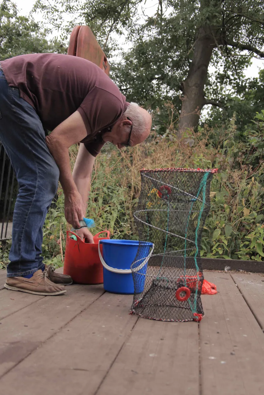 Bob Ring digs through a bucket for a clip while standing on an angler platform next to a lake. Photo by Jackie Turner.
