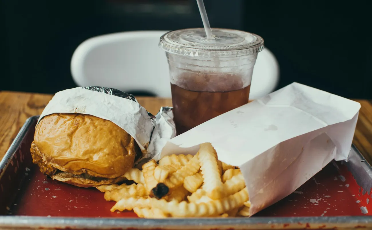 A tray of fast food including a burger, fries, and a drink. Photo by Christopher Williams on Unsplash.