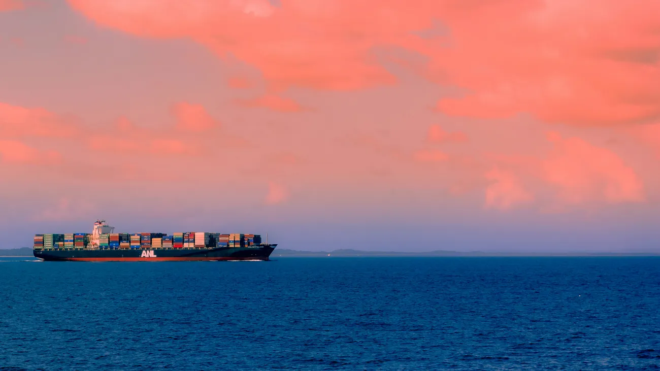 A cargo ship sailing off into a sunset. Photo by Anastasios Antoniadis via Unsplash.