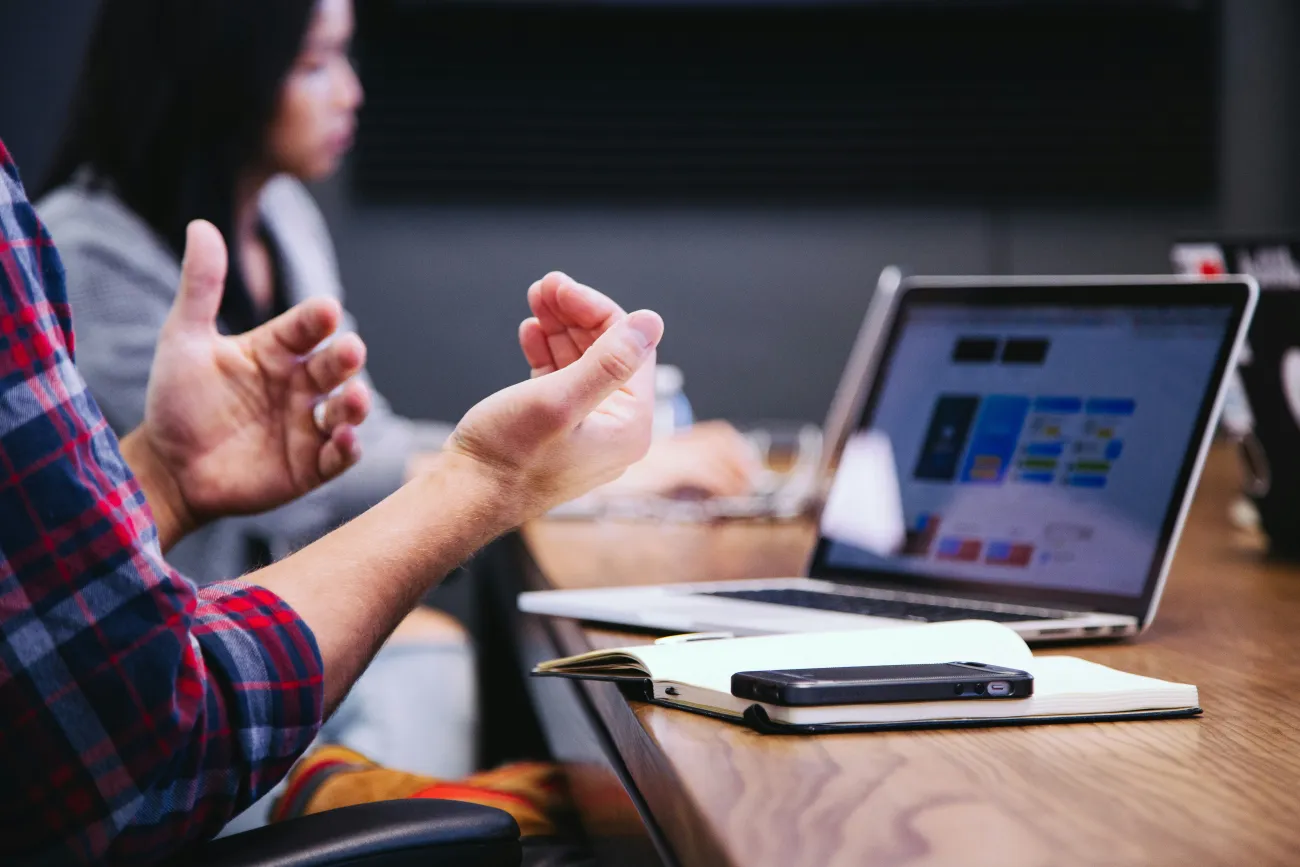 A man at a table gesticulating with his hands. Photo by Headway via Unsplash.