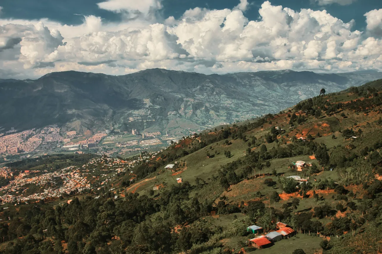 A hillside in Medellín with houses sprawled in the valley in the distance and mountains beyond that. Photo by Jan Brennenstuhl via UnSplash.