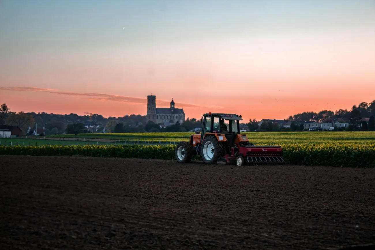 Photo of tractor in field with village in background. Credit: Nicolas Veithen via Pexels