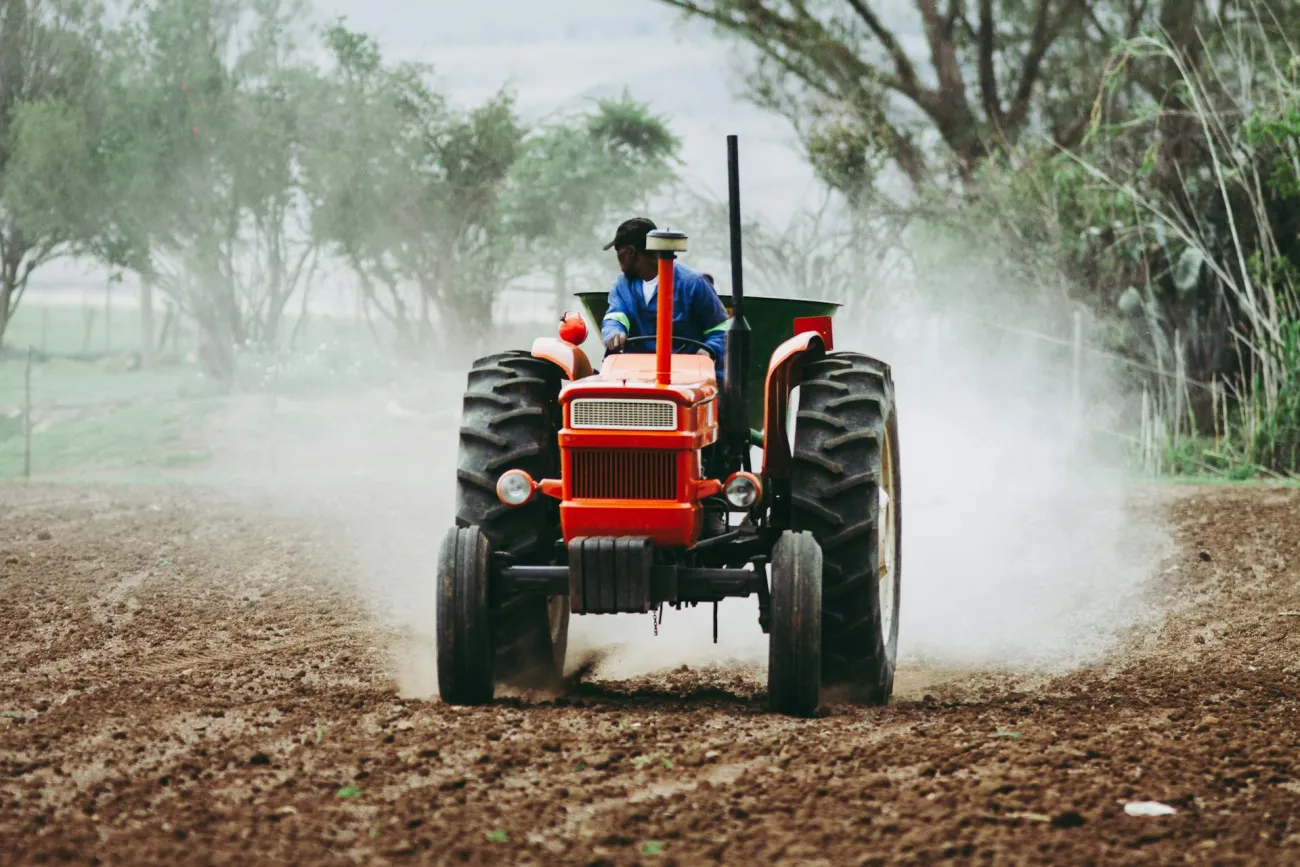 Farmer sitting on tractor driving through field. Credit: Marools via Pexels