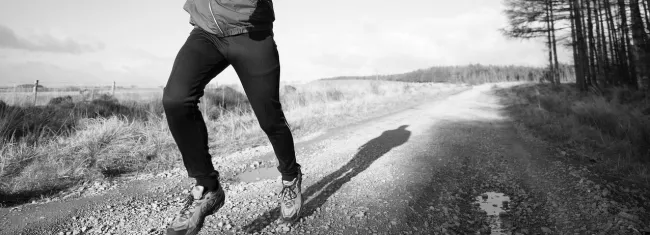 Photo of a man running, centered on his feet on a dirt road.