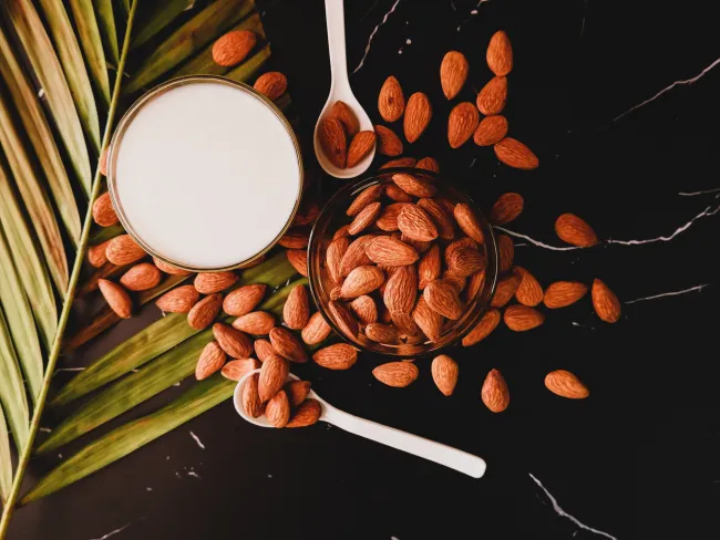 A cup of almonds and a cup of almonds milk. Photo by dhanya purohit via Unsplash.