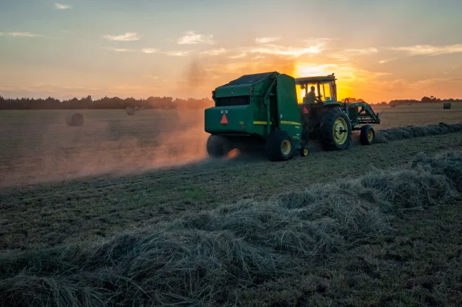A tractor emitting fumes whilst ploughing a field. Photo by Jed Owen via Unsplash