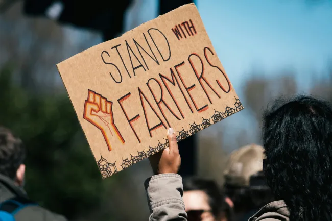 Photo of a protest sign which reads “Stand with Farmers”. Image by Gayatri Malhotra via Unsplash
