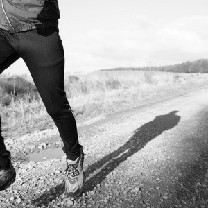 Photo of a man running, centered on his feet on a dirt road.