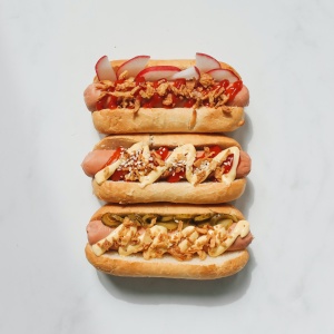 Image of three hot dogs with various toppings on white surface. Photo by Polina Tankilevitch via Pexels.